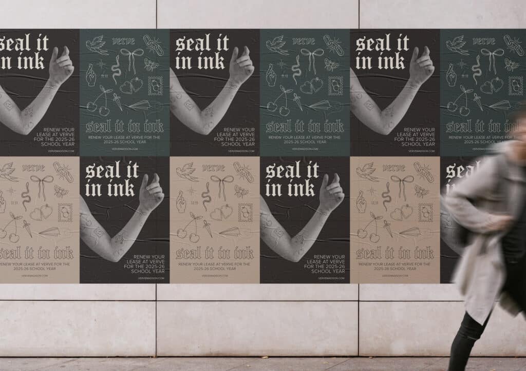 A wall displays a series of posters with illustrations and the text "seal it in ink." A person is walking by in the foreground, slightly blurred.