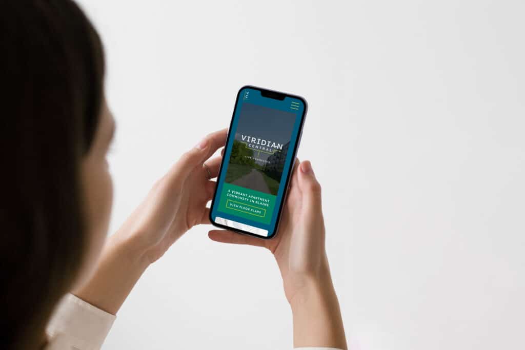 A person holding a smartphone displaying a website with the heading "Viridian Centennial." The site's interface has options for "Explore" and "Take a Tour.