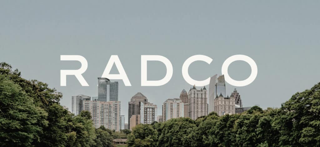 Skyline view of a city with tall buildings and green trees. The word "RADCO" is prominently displayed across the image.