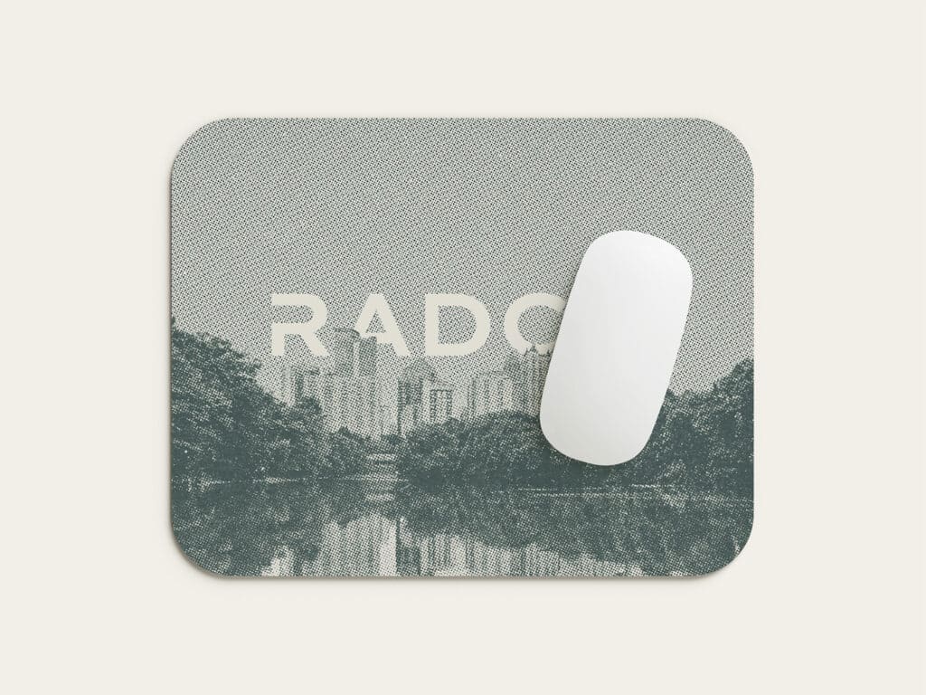 Mouse pad with a city skyline and trees reflected on a river, featuring the text "RADO." A white computer mouse is placed on top.