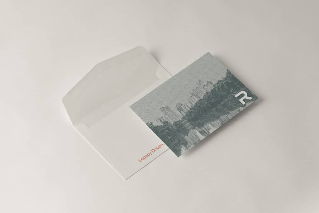 Envelope partially open with a card inside. The card features a grayscale image of a cityscape with the letter "R" in the corner. The envelope says "Legacy Driven" in red text.