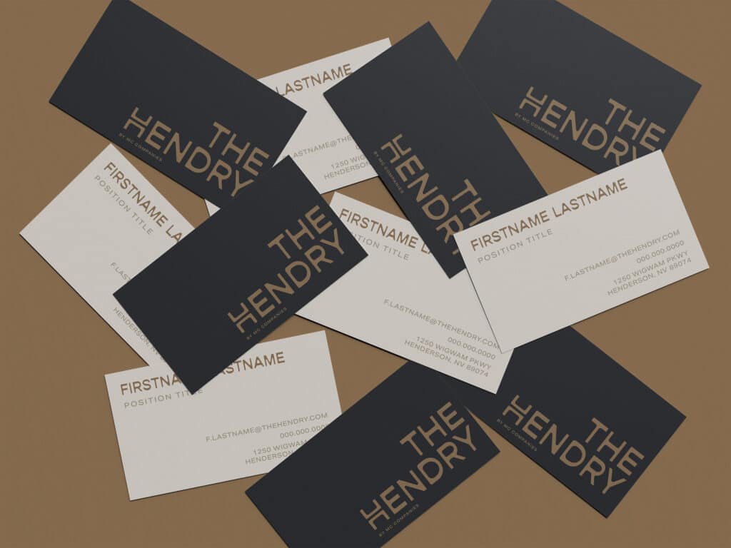 Scattered black and white business cards for "The Hendry," showing placeholders for name, position, contact details, and website on a brown surface.